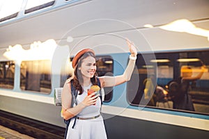 Backpack traveler woman waving hand at train station platform summer holiday traveling concept. Female tourist greeting and enjoy