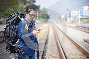 Backpacker asian woman in casual dress and bag on,wait for the railway train hand hold smart mobile phone with copy space