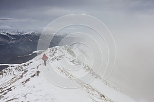 Backpacker climbing a mountain narrow snowy ridge in winter