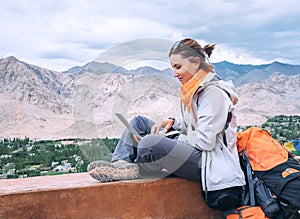 Backpacker with laptop sits on the top view point under mountain