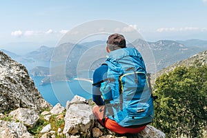 Backpacker man sitting on clifftop and enjoying the Mediterranean Sea Oludeniz town Bay during Lycian Way trekking walk. Famous