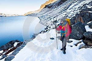 Backpacker man standing snow mountain trail above lake.