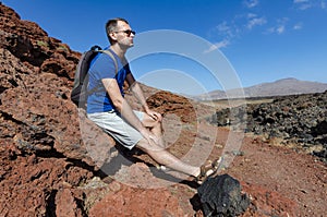 A backpacker resting on a rock while trekking among volcanic landscape