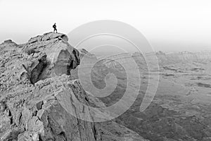 Backpacker tourist standing mountain cliff edge, black and white