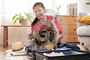 Backpacker travel of journey, asian young woman playing with her cat, pet while check list, packing or prepare clothes into
