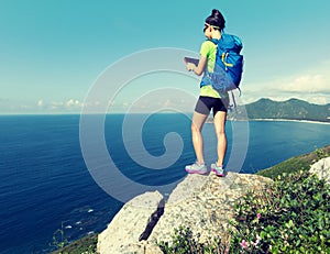 Backpacker use digital tablet on seaside mountain cliff edge