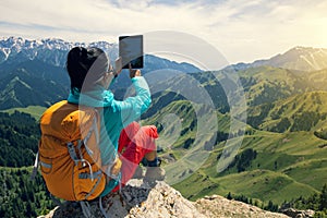 backpacker using digital tablet taking photo on mountain top cliff edge