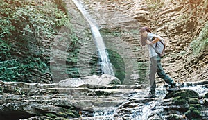 Backpacker woman crossing mountain creek in front of waterfall.