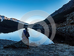 Backpacker woman sitting at a mountain lake winter