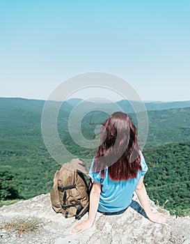 Backpacker woman sitting on peak of cliff in summer.