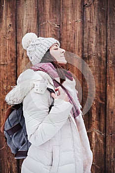 Backpacker woman walking in city during winter while snowing. relaxed woman enjoying outdoors with eyes closed over wood