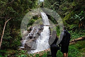 Backpackers couple holding hands facing a beautiful waterfall in Chiang Mai (Thailand