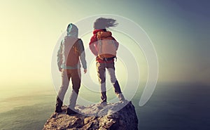 Backpackers stand on sunrise seaside mountain top rock edge photo