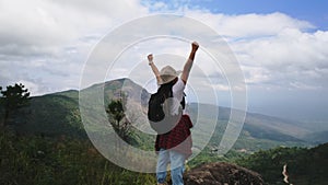 Backpacking female hiker stands on top of the mountain with raised arms and enjoying the view. journey and success concept