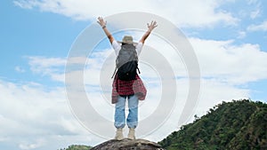 Backpacking female hiker stands on top of the mountain with raised arms and enjoying the view. journey and success concept