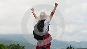 Backpacking female hiker stands on top of the mountain with raised arms and enjoying the view. journey and success concept