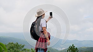 Backpacking female hiker stands on top of the mountain with raised arms and enjoying the view. journey and success concept