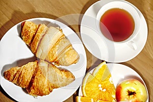 Backround continental breakfast with gold french croissants, fruits and cup of tea on wooden table. Great choice on morning. Tasty