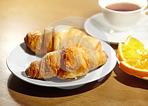 Backround continental breakfast with gold french croissants, fruits and cup of tea on wooden table. Great choice on morning. Tasty