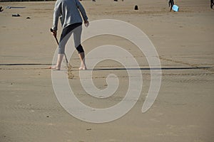 Backshot of a person drawing with a wooden stick on the sandy beach