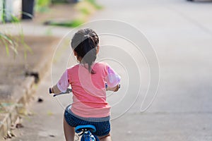 Backside of asian toddler girl child learning to ride bicycle in sunny summer day, kid cycling at park, baby sport concept