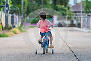 Backside of asian toddler girl child learning to ride bicycle in sunny summer day, kid cycling at park, baby sport concept