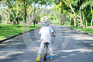 Backside of Asian 2 years toddler boy child wearing safety helmet learning to ride first balance bike