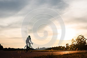 Backside of cyclist ride bicycle on sunset time in public park. Sport and active life concept