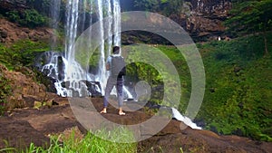 Backside guy with backpack stands on rock watches waterfall