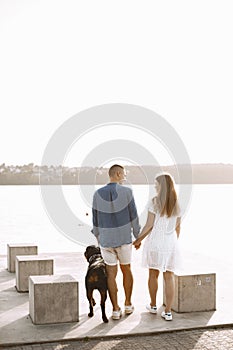 Backside photo of a romantic couple with their rotweiller near the lake