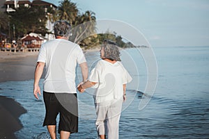 Backside of romantic Asian senior couple hand in hand while walking on summer beach sunset. Travel leisure and activity after