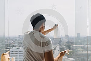 Backside view of asian Thai man wiping window glass in room apartment with city view, keep glass sparking clean