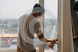 Backside view of asian Thai man wiping window glass in room apartment with city view, keep glass sparking clean