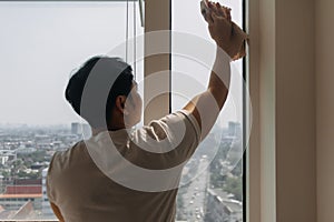 Backside view of asian Thai man wiping window glass in room apartment with city view, keep glass sparking clean