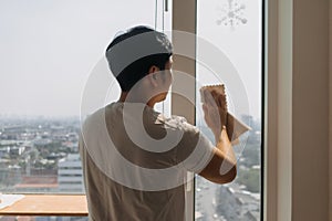 Backside view of asian Thai man wiping window glass in room apartment with city view, keep glass sparking clean