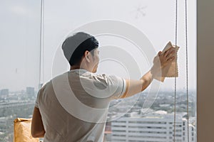 Backside view of asian Thai man wiping window glass in room apartment with city view, keep glass sparking clean