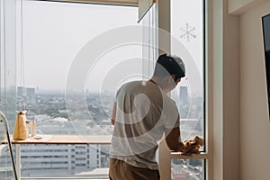 Backside view of asian Thai man wiping window glass in room apartment with city view, keep glass sparking clean