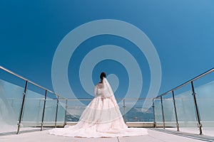 Backside view of bride stands on balcony in white dress with long train
