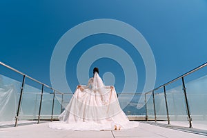 Backside view of bride stands on balcony in white dress with long train