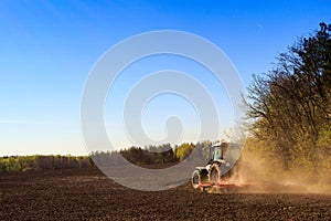 backside view cultivator on ploughed field by spring wood