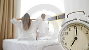 Backview on disfocused young loving couple stretching arms after waking up on bed and looking outside windows in bedroom