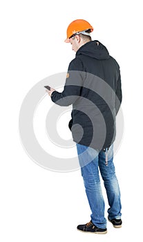 Backview of an engineer in construction helmet stands and using