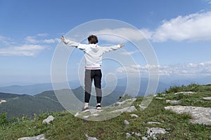 Backview of girl with hands up standing on peak of mountains looking on blue sky and mountain landscape.