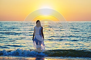 Backview of a girl in white dress walking in sea waves.