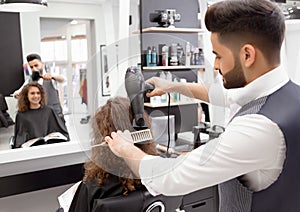 Backview of hairstyler doing hairdress for smiling curly female client.