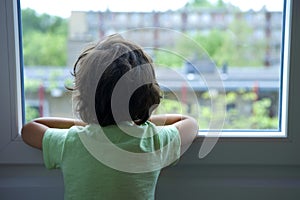 Backview of a lonely little boy looking out of the window