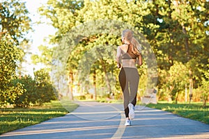 Backview of sporty girl running along racetrack in the city park.