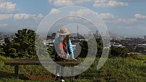 Backview of young tourist woman looking view with Auckland city skyline with Auckland Sky Tower from Mt. Eden at sunset New