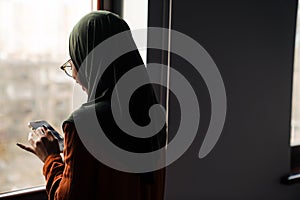 Backview of young woman in hijab looking on her phone