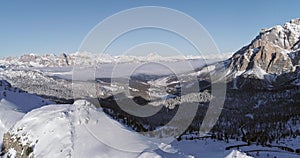 Backward aerial to snowy valley with woods forest and road at Valparola pass.Sunny sunset or sunrise, clear sky.Winter